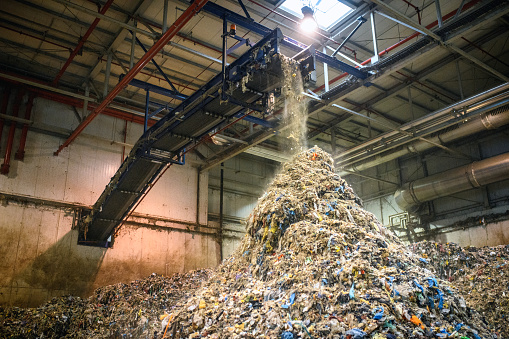 Low angle view of recyclables falling from conveyor belt within waste management facility onto massive pile that will be further processed.