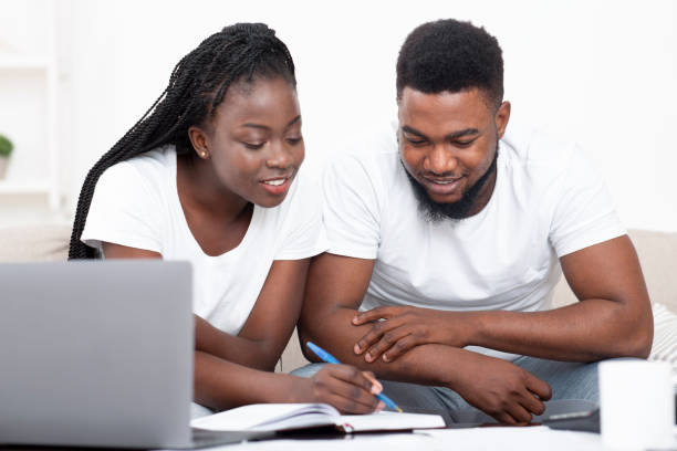 Young black couple planning budget together at home and writing notes