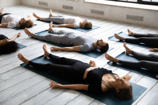 giovani che meditano nella posa di savasana, praticando yoga a lezione - sdraiarsi foto e immagini stock