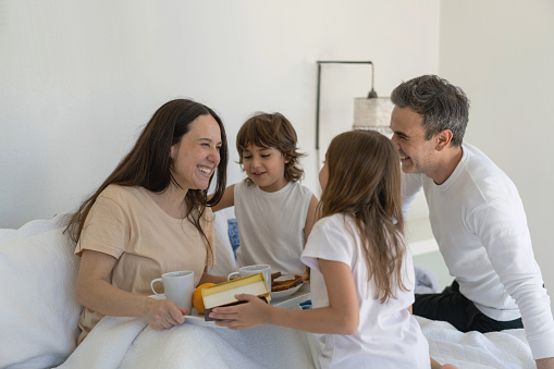 Beautiful father with his two kids surprising mother with breakfast in bed for mother's day