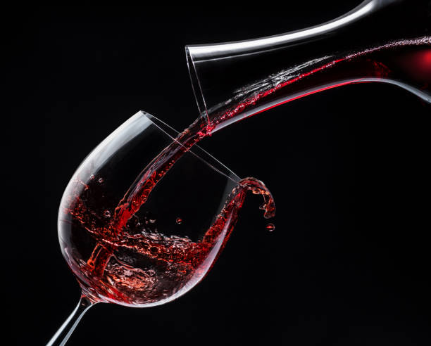 istock Red wine is poured into a wine glass on a black background. 1199688161