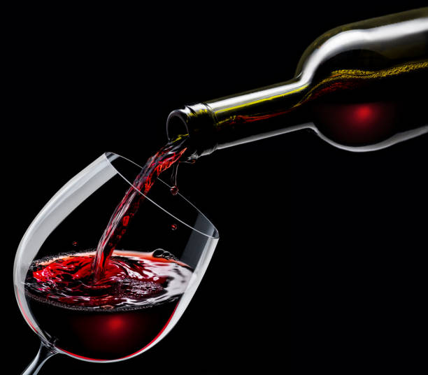 istock Red wine is poured into a wine glass on a black background. 1199688193