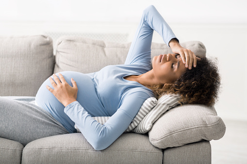 Pregnancy and migraine. Woman suffering from severe headache, lying on sofa at home