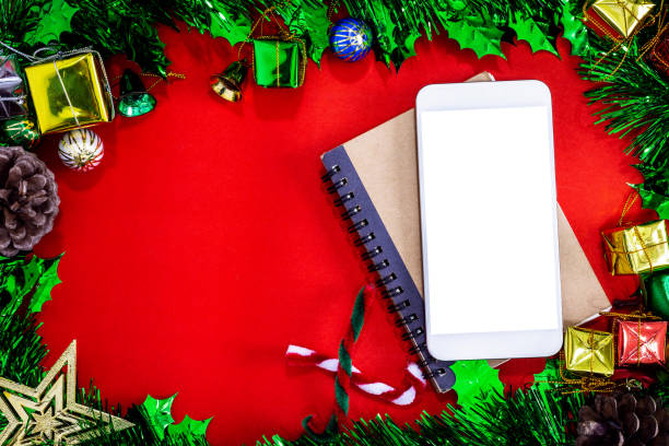 istock Top view image of Christmas festive decorations with empty smartphone,notebook and pencil on red paper background, New Year concept. 1199690482