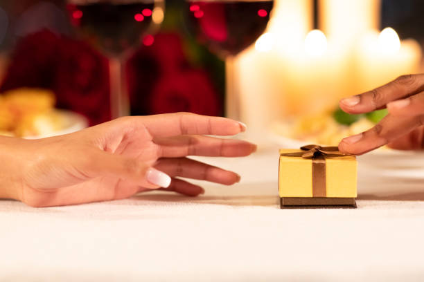 homme poussant la boîte de cadeau à la petite amie sur la table de restaurant, plan rapproché - anniversary couple rose black photos et images de collection