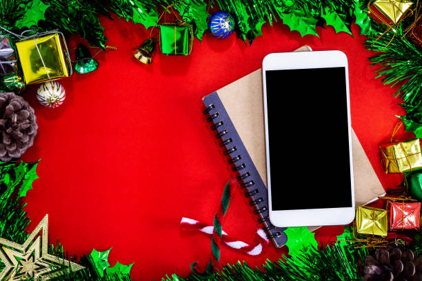 istock Top view image of Christmas festive decorations with empty smartphone,notebook and pencil on red paper background, New Year concept. 1199691379