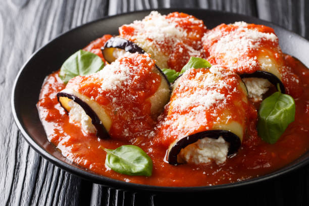 involtini di melanzane al forno con ricotta in salsa di pomodoro e serviti con parmigiano e basilico da vicino in un piatto. orizzontale - eggplant parmesan cheese baked cheese foto e immagini stock