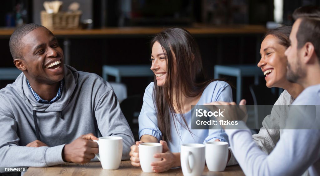 Multiracial friends girls and guys having fun laughing drinking coffee Multiracial friends girls and guys having fun laughing drinking coffee tea in coffeehouse, happy diverse young people talking joking sitting together at cafe table, multicultural friendship concept Friendship Stock Photo
