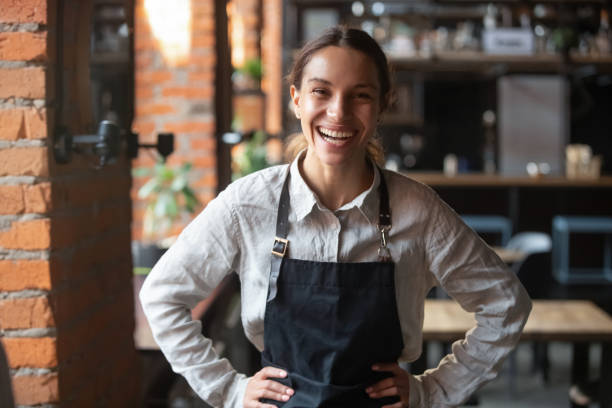 istock Cheerful young waitress wearing apron laughing looking at camera 1199696862