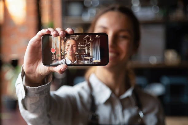 feliz joven camarera vlogger sosteniendo smartphone grabación de video blog - dispositivo de información móvil fotos fotografías e imágenes de stock