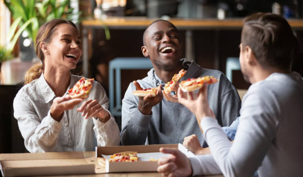 joyful multicultural friends laughing sharing takeaway pizza meal together - pizza eating african descent lunch imagens e fotografias de stock