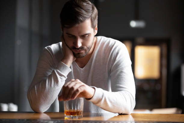 Upset man drinker alcoholic sitting with glass drinking whiskey alone Upset young man drinker alcoholic sitting at bar counter with glass drinking whiskey alone, sad depressed addicted drunk guy having problem suffer from alcohol addiction abuse, alcoholism concept addiction stock pictures, royalty-free photos & images