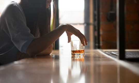 Sad desperate woman drinker alcoholic holding whiskey glass drinking alone sit at bar counter, upset stressed girl addicted to alcohol feel lonely frustrated suffer from alcoholism problem concept