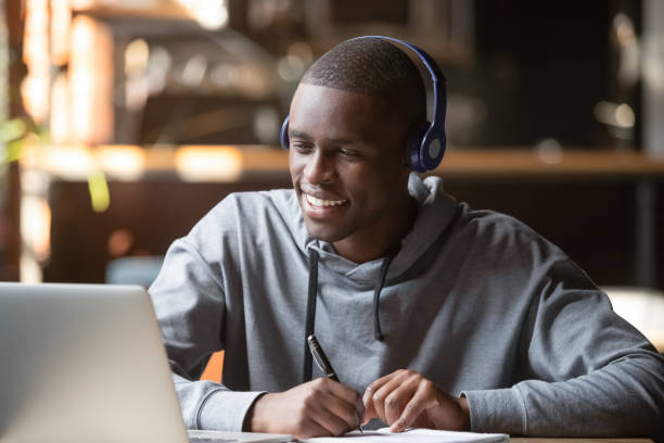 smiling african young man student wearing headphones study online - cyberspace support computer assistance imagens e fotografias de stock