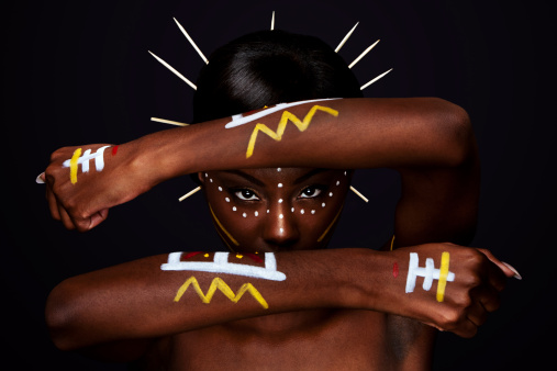 Beautiful cultural tribal African female face with arms and hands in front, yellow, red and white makeup cosmetics lines dots, sticks in hair.