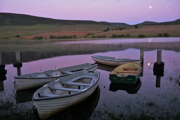 Moonlight reflection Pentland Hills, Scotland - 14 July 2019: A mid-summer evening shot, taken after sunset, of anglers' boats moored on the still water of Threipmuir reservoir in the Pentland Hills outside Edinburgh. The moon is reflected on the still water surface. fly fishing scotland stock pictures, royalty-free photos & images