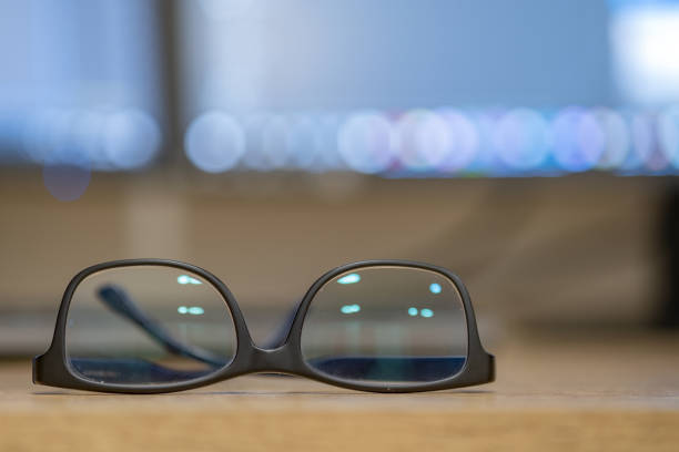 istock Closeup of protective glasses on an empty desk with blurred computer screen on background. 1199706150