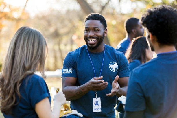 Mid adult volunteer talks with friends during event Happy African American man gestures while talking with two friends during a community cleanup event. coordination photos stock pictures, royalty-free photos & images