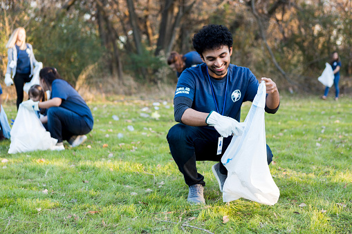 Happy young man smiles while picking up litter during a community cleanup day. He and his neighbors are cleaning up their community park.