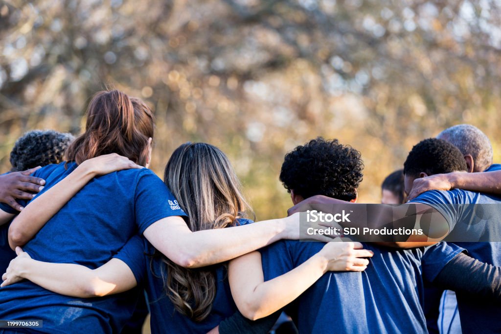 Friends linking arms in unity Diverse group of friends cleanup a park during a charity event. They are standing with their arms around one another. Community Stock Photo