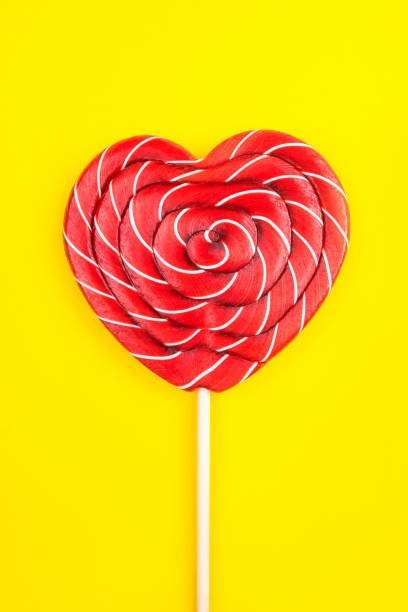 una piruleta en forma de corazón sobre un fondo amarillo. - flavored ice lollipop candy affectionate fotografías e imágenes de stock