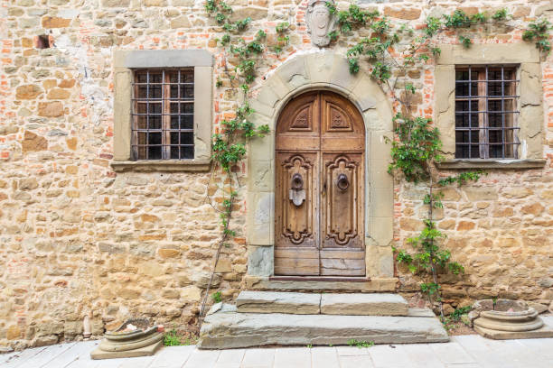 Arched doorway with two windows and climbing ivy. Grand wooden door with ivy climbing the stone walls in the medieval town of Volpaia, Italy. rustic door stock pictures, royalty-free photos & images
