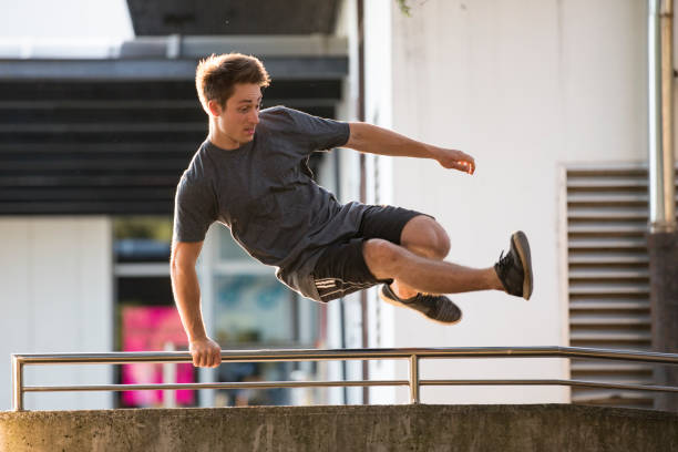 junger erwachsener mann springt über einen zaun auf der city street - le parkour stock-fotos und bilder