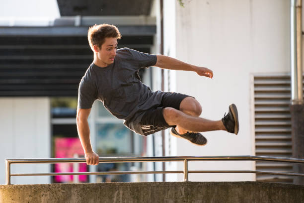 joven adulto saltando sobre una valla en city street - carrera urbana libre fotografías e imágenes de stock
