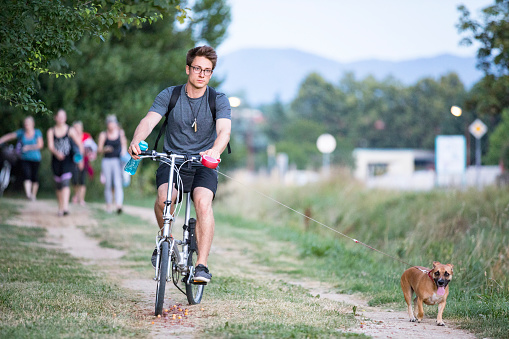 Young Adult Man Walking His Dog With a Bicycle in Public Park.