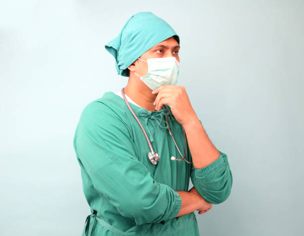 mężczyzna chirurg azji, chirurg pokazano stetoskop sobie maskę chirurga, na niebieskim tle w studio. - surgeon isolated paramedic operating room zdjęcia i obrazy z banku zdjęć