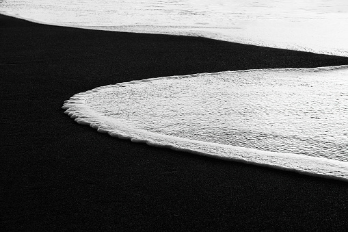 curvy wave in the sand shore of beach in black and white