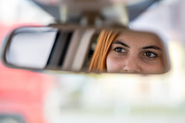 istock Young woman driver checking rear view mirror looking backwards while driving a car. 1199714298