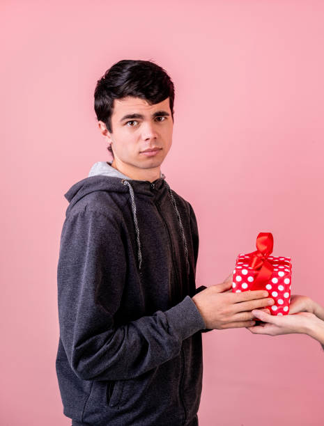 istock young man feeling confused and puzzpled getting a gift box from female hands isolated on pink background 1199716708
