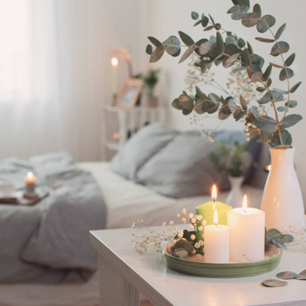 burning candles and eucalyptus in  vase in white bedroom