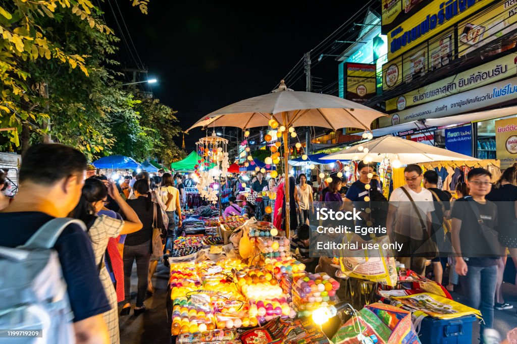 Night market in Chiang Mai city shortly after sunset. Chiang Mai, Thailand - 3.11.2019: Night market in Chiang Mai city shortly after sunset. Tourist are walking on the road. Thai sellers in the stall on side. Souvenirs and streetfood, summer day. Chiang Mai City Stock Photo Night market in Chiang Mai city shortly after sunset. Chiang Mai, Thailand - 3.11.2019: Night market in Chiang Mai city shortly after sunset. Tourist are walking on the road. Thai sellers in the stall on side. Souvenirs and streetfood, summer day. Chiang Mai City Stock Photo