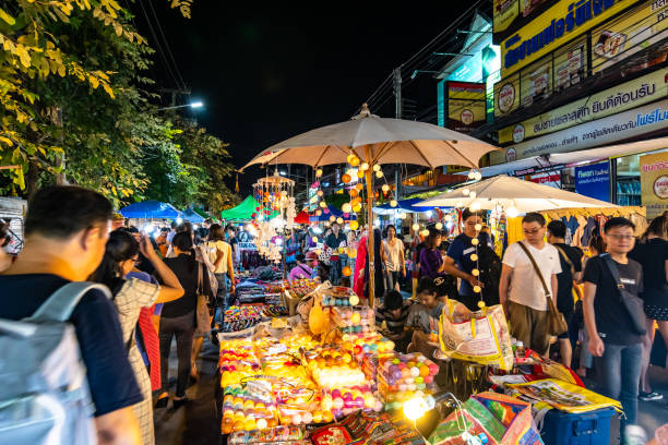 Night market in Chiang Mai city shortly after sunset. Chiang Mai, Thailand - 3.11.2019: Night market in Chiang Mai city shortly after sunset. Tourist are walking on the road. Thai sellers in the stall on side. Souvenirs and streetfood, summer day. chiang mai city stock pictures, royalty-free photos & images