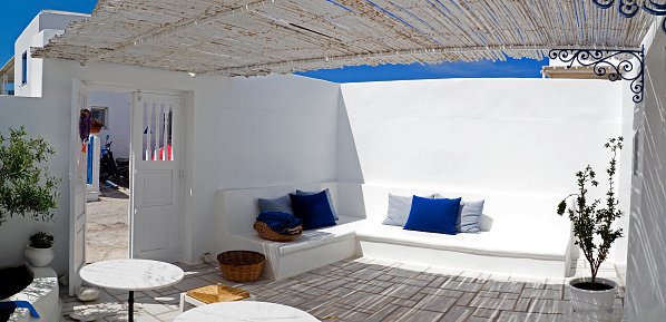 One of the charms of Mykonos, the Greek island of Cyclades, are the small terraces with their colorful tables and chairs on the ground floor of the white houses of the narrow cobbled streets.
