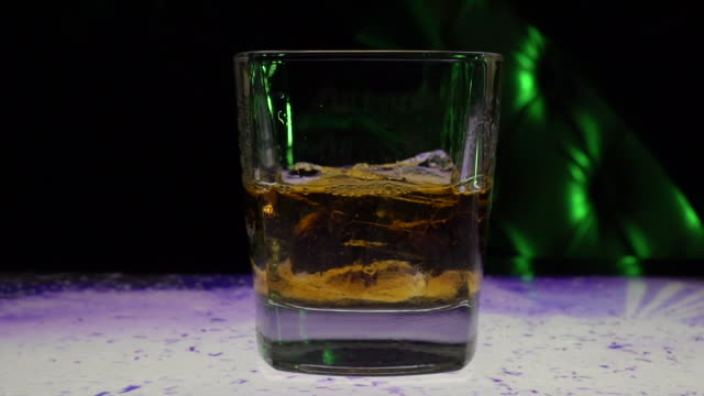 Unrecognizable person taking whiskey glass with whiskey and ice cubes in it from bar counter
