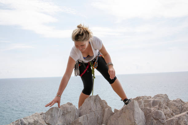 le jeune grimpeur de roche de femme grimpe à travers les roches au dessus d'une montée au-dessus de la mer - mountain climbing rock climbing motivation awe photos et images de collection