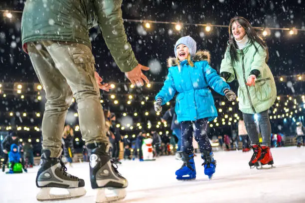 Photo of Skating rink. Happy family on the ice rink. Mom and dad teach daughter to skate.