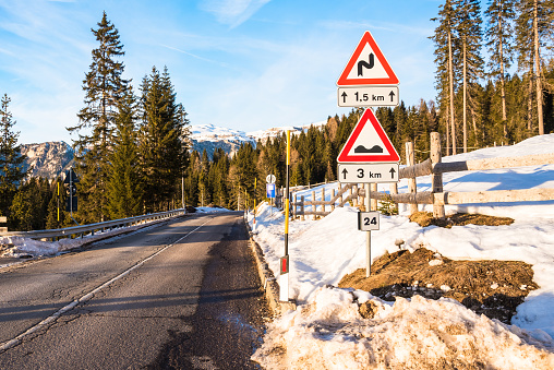 Triangular warning signs along a mountain road cleared of snow in the Alps on a sunny winter afternoon