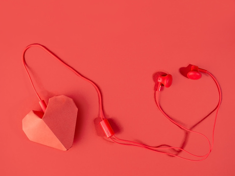 listen to the music of love. headphones and a red paper heart on a bright background. song of the heart.