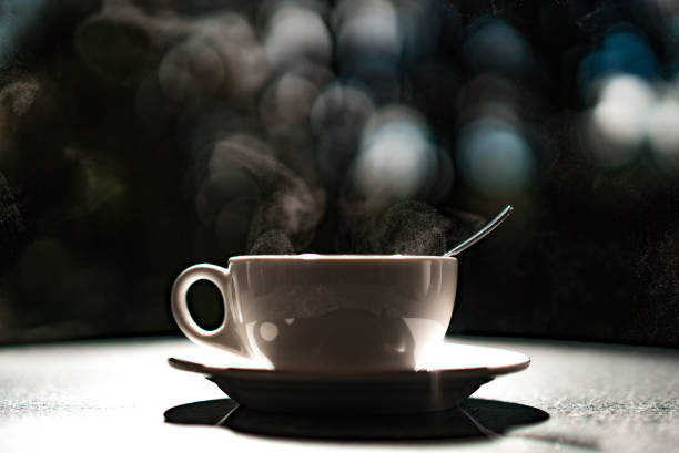 istock White cup with hot liquid and steam on black blurred background. 1199743592