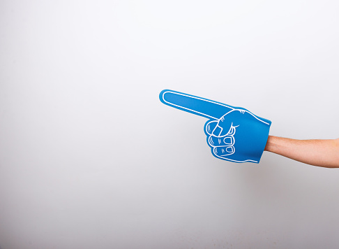 Handsome fan hand glove with foam finger, pointing away over white wall background