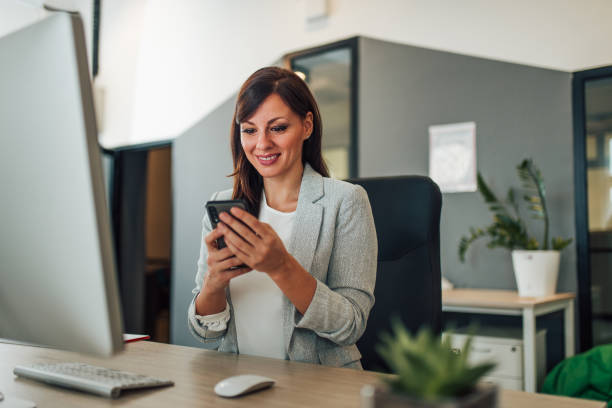 istock Portrait of a smiling woman using smart phone at modern workplace. 1199745934