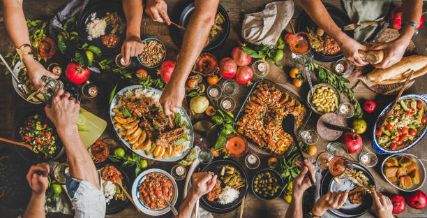 Flat-lay of peoples hands and Turkish foods over rustic table Turkish cuisine family feast. Flat-lay of peoples hands and lamb chops with quince, beans, salad, babaganush, rice pilav, pumpkin dessert, lemonade over rustic table, top view. Middle East cuisine dinner party stock pictures, royalty-free photos & images