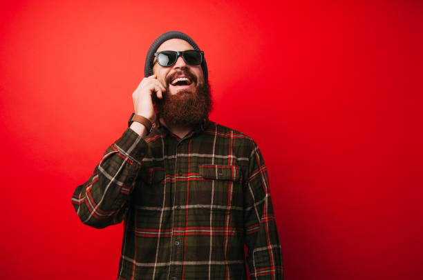 istock Cheerful man with beard talking on phone over red background 1199748900