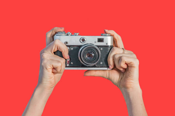 istock Woman hands holding retro camera isolated on red background 1199748903