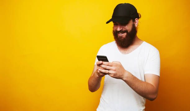 istock Happy bearded man in white t-shirt texting message over yellow background 1199749716