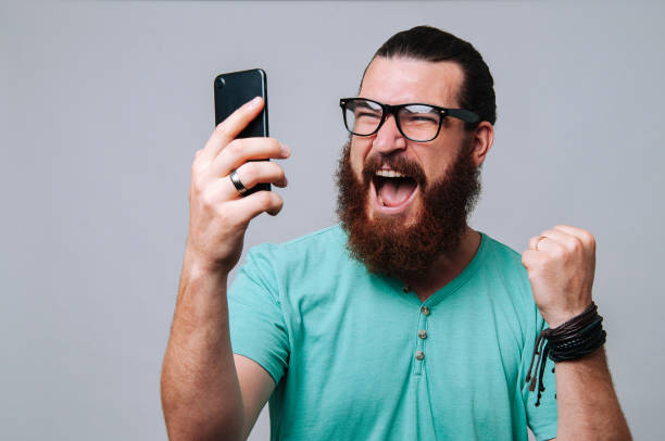 istock Bearded hipster man looking at phone and celebrating success 1199751118